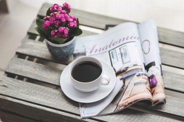Coffee sitting on a magazine beside flowers